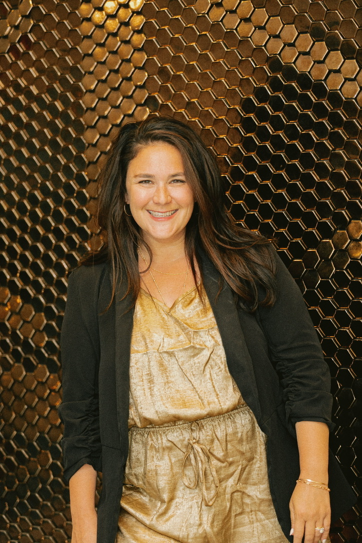Aly Carter smiling in front of a gold honeycomb wall