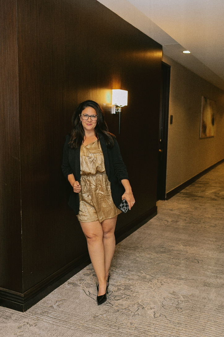 Aly Carter walking down a hotel corridor in a gold romper